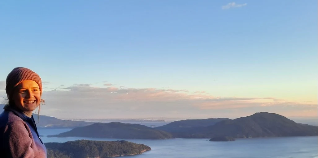 Sam Wing smiling at the edge of the frame, with the islands of Howe Sound and a soft sunset behind